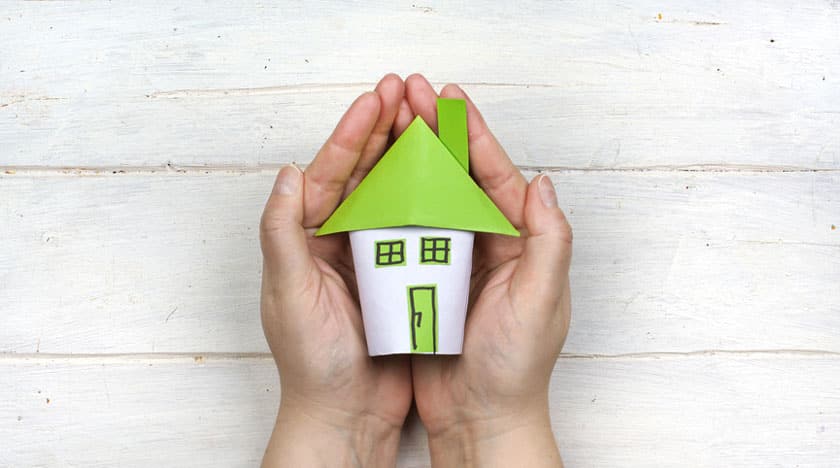 Image symbolique : une maison en papier vert dans une main représente la biologie de la construction.