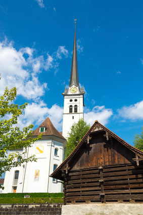 Ein Kirchturm mit einer verborgener Mobilfunkantenne vor blauem Himmel.