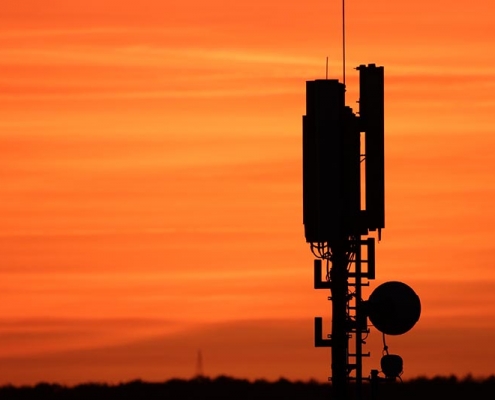 Ein Mobilfunkmast zeichnet sich als Silhouette vor einem orangefarbenen Himmel ab.