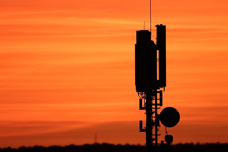 Ein Mobilfunkmast zeichnet sich als Silhouette vor einem orangefarbenen Himmel ab.