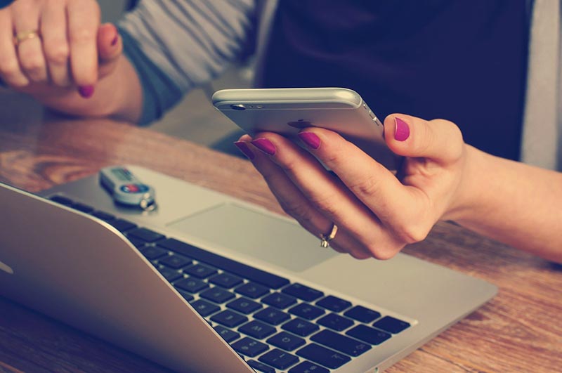 Une femme tient un téléphone portable à côté d'un ordinateur portable.