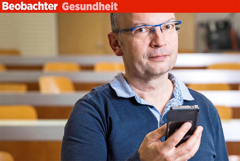 Martin Röösli hält ein Handy vor einem Hörsaal zum Thema Elektrosmog.