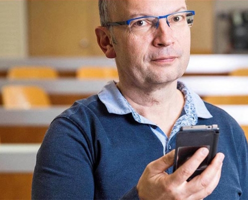 Martin Röösli hält ein Handy vor einem Hörsaal zum Thema Elektrosmog.