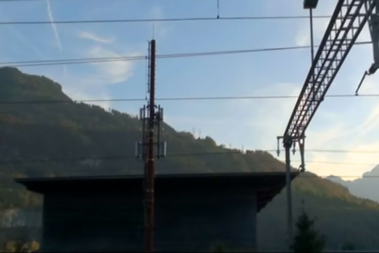Une vue d'une gare avec un pylône de téléphonie mobile et des montagnes en arrière-plan.