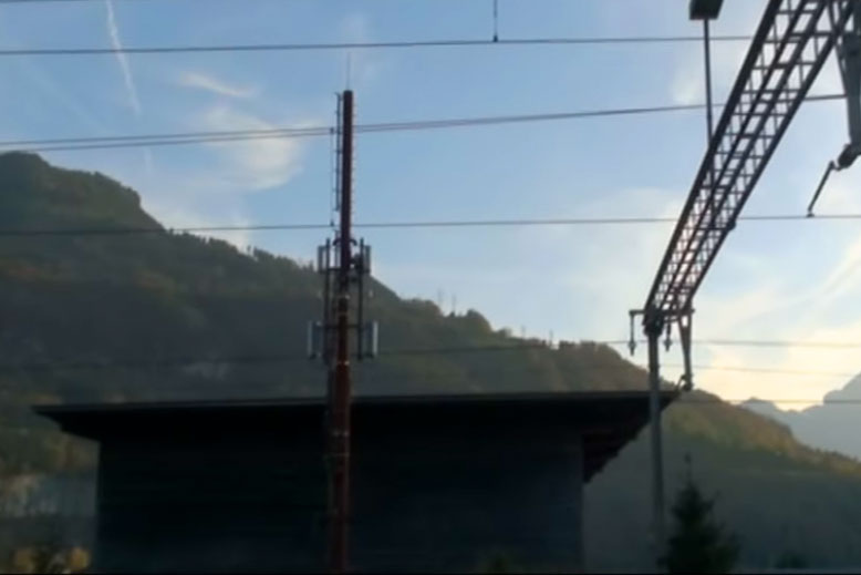 Ein Blick auf einen Bahnhof mit Mobilfunkmast und Bergen im Hintergrund.