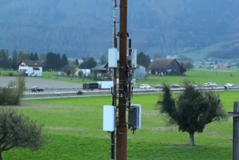 Ein 5G-Mobilfunkmast an einer Bahnstrecke mitten auf einem Feld.