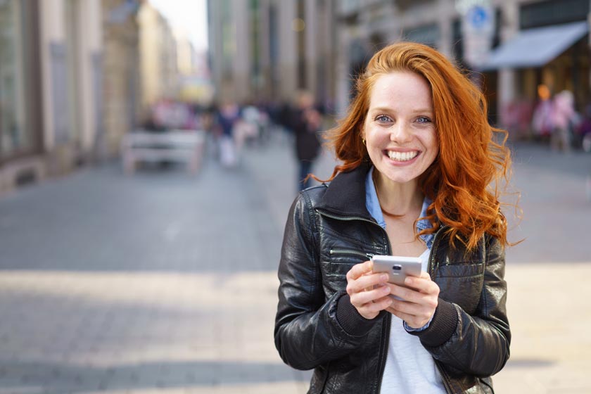 Eine junge Frau hält ein Mobiltelefon in einer Stadt.