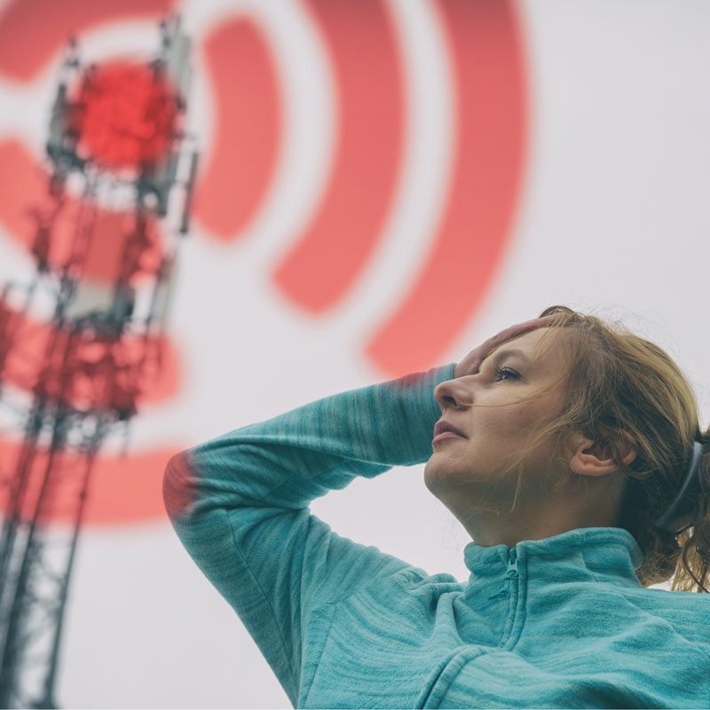 Une femme lève les yeux vers un pylône de téléphonie mobile.