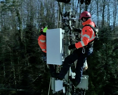 Deux hommes travaillent sur un pylône de téléphonie mobile 5G dans la forêt.