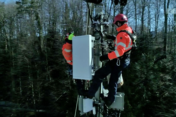 Deux hommes travaillent sur un pylône de téléphonie mobile 5G dans la forêt.