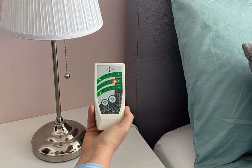 Eine Person hält ein Elektrosmog-Messgerät vor einem Bett.
