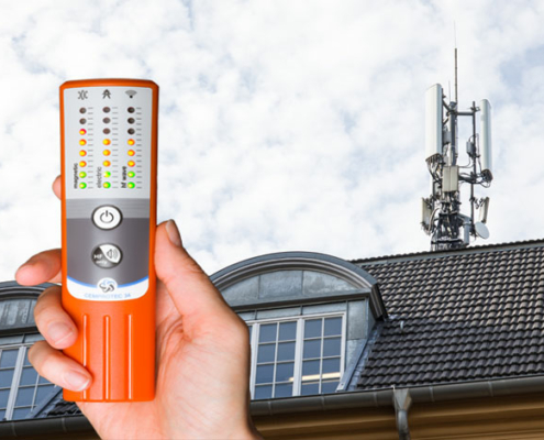 Ein Cemprotec 34 Elektrosmog-Messgerät vor einem Haus mit Handy-Antenne.