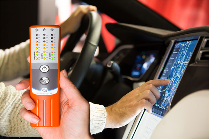 Eine Person hält ein Cemprotec 34 Hochleistungs-Elektrosmog-Messgerät in einem Auto.