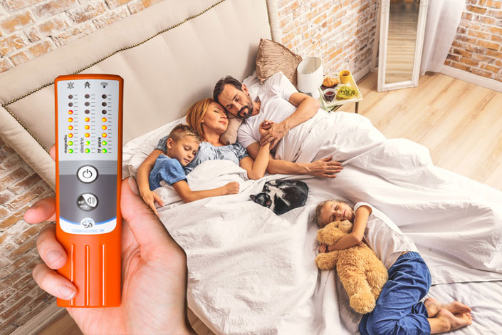 Une famille au lit avec un appareil de mesure de l'électrosmog haute performance Cemprotec 34.