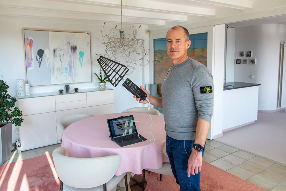 Un homme mesure l'électrosmog devant une table avec un ordinateur portable.